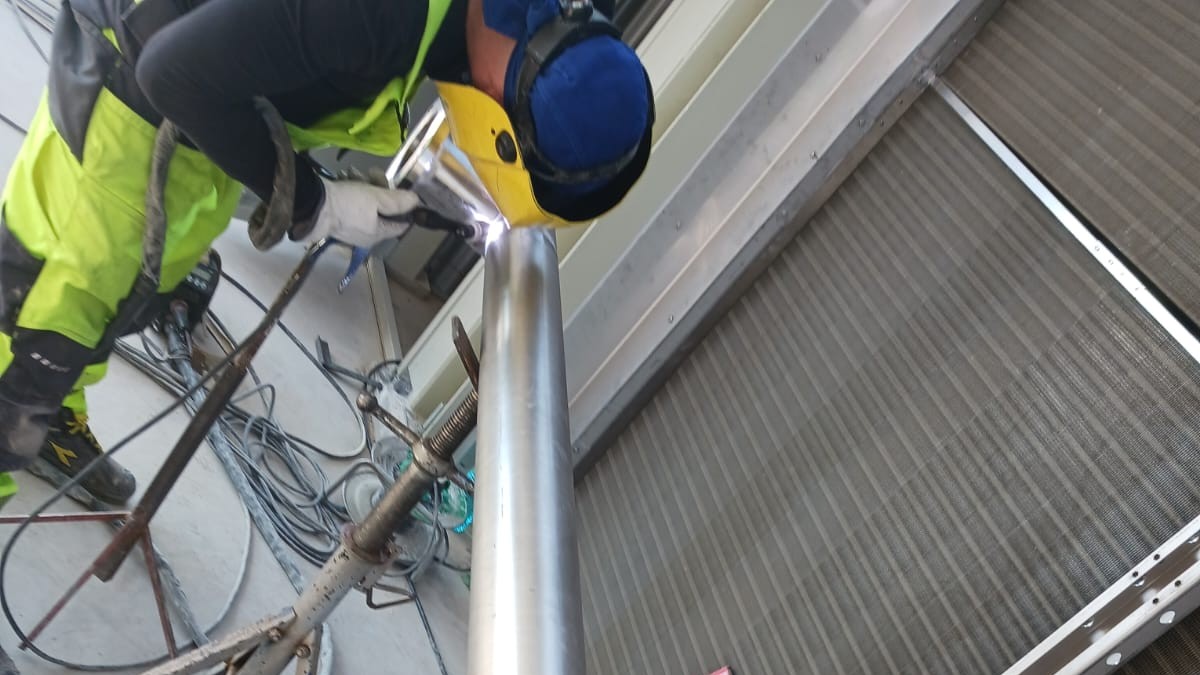 Sudor care sudează o țeavă de inox pe capre, vedere din lateral