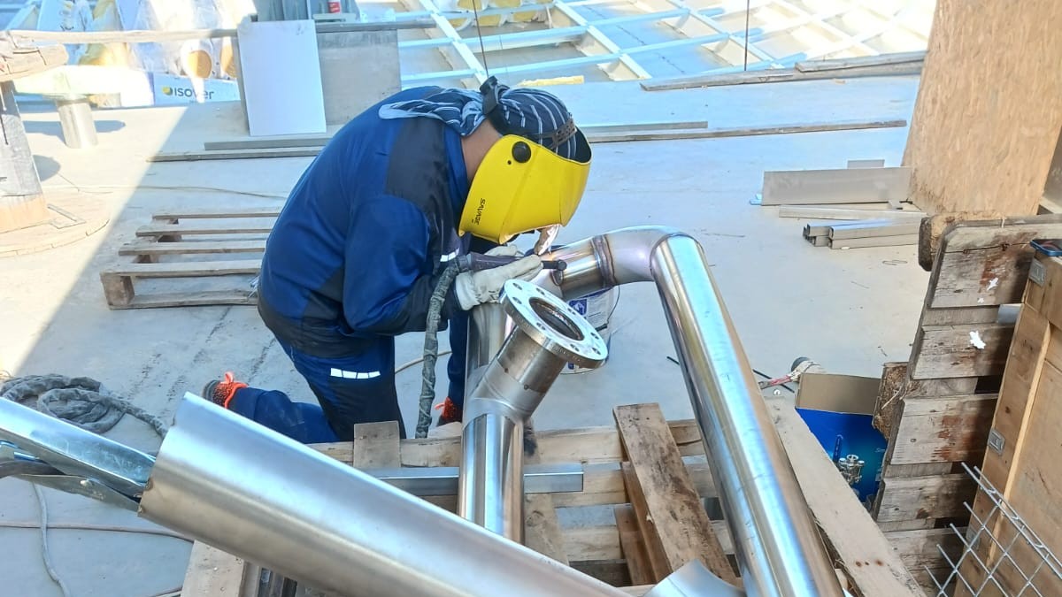 Sudor care sudează o țeavă de inox într-un spațiu exterior industrial